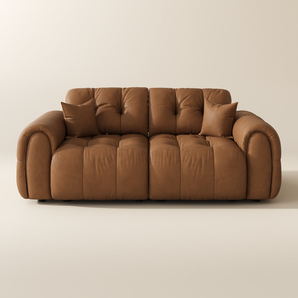 Brown top-grain leather tufted modular sofa with two pillows on a plain background
